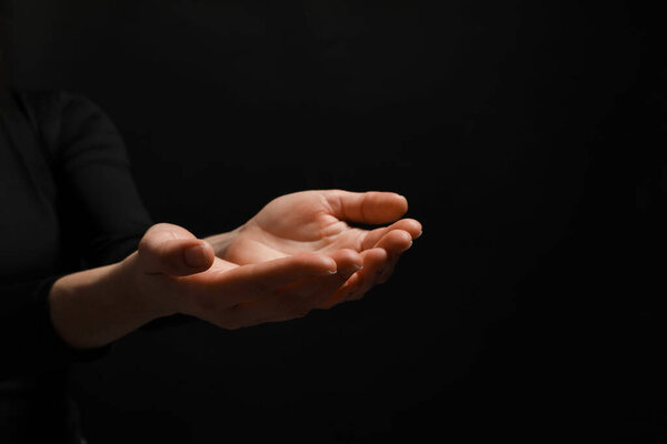 Religion. Woman with open palms praying on black background, closeup. Space for text