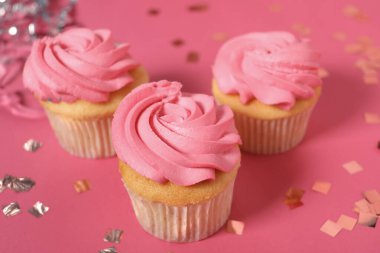 Parlak kremalı lezzetli kekler ve pembe masada konfeti, yakın plan.