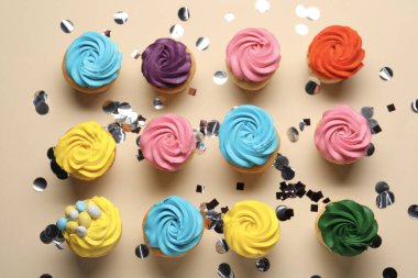 Parlak kremalı lezzetli kekler ve bej arka planda konfeti.