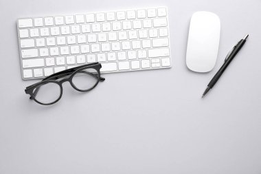 Ofis işyeri. Klavye, fare, gözlük ve kalem açık gri masada, düz yerde. Metin için boşluk