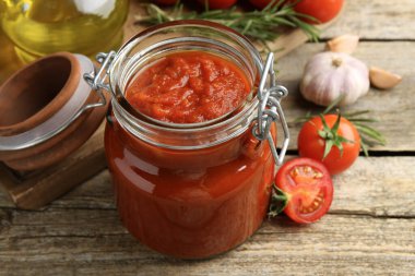 Kavanozda ev yapımı domates sosu ve ahşap masada taze malzemeler, yakın plan.