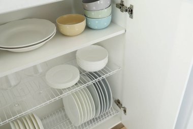 Dolabın içindeki raflarda temiz tabaklar, kaseler ve bardaklar.
