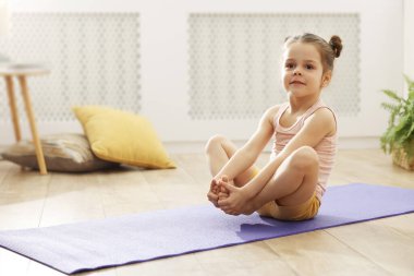 Evdeki minderde yoga yapan küçük tatlı kız.