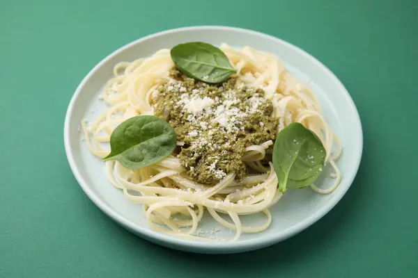Tasty pasta with spinach, cheese and sauce on green table