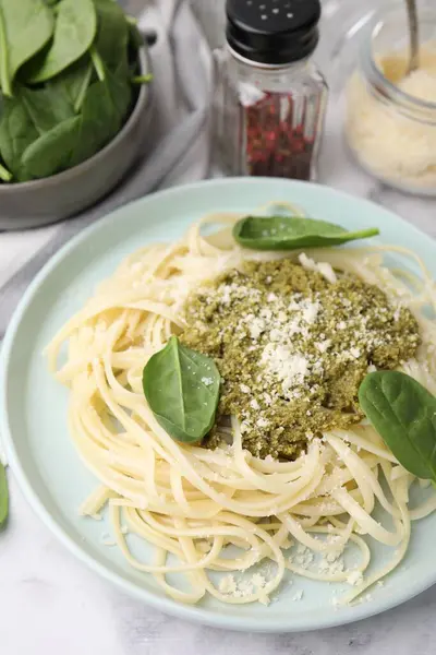 Tasty pasta with spinach, cheese and sauce on white marble table