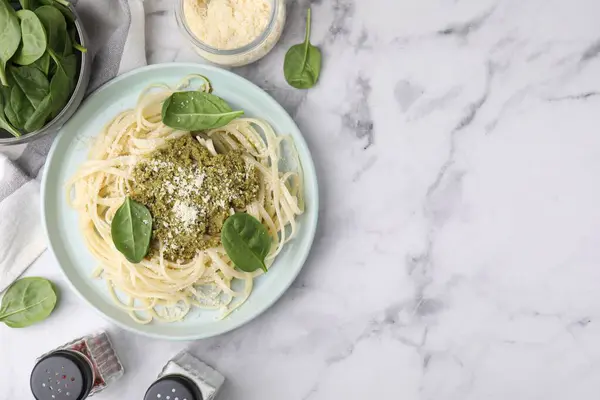 Tasty pasta with spinach, cheese and sauce on white marble table, flat lay. Space for text