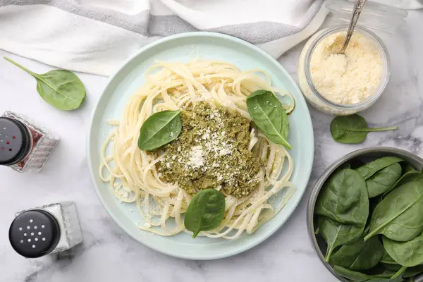 Tasty pasta with spinach, cheese and sauce on white marble table, flat lay