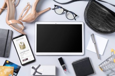 İnternetteki mağaza. Tablet, akıllı telefon, kırtasiye, kredi kartları, alışveriş arabası ve açık gri arka planda aksesuarlar, düz uzanma