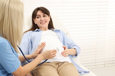 Hamilelik kontrolü. Steteskoplu bir doktor klinikte bebeğin kalp atışlarını dinliyor. Metin için boşluk