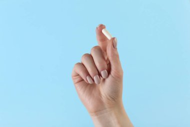 Açık mavi arka planda vitamin kapsülü tutan kadın, yakın plan. Sağlık takviyesi