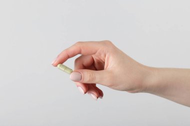 Gri arka planda vitamin kapsülü tutan kadın, yakın plan. Sağlık takviyesi