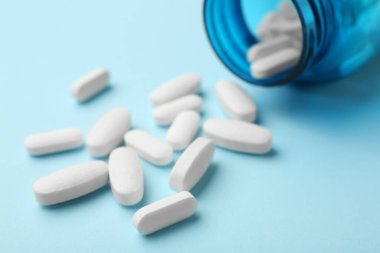 Açık mavi arka planda vitamin hapları ve şişe, yakın plan.