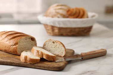 Hasır ekmek sepeti, taze fırınlanmış somunlar ve mutfaktaki beyaz mermer masada bıçak.