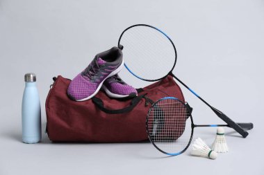 Badminton seti, çanta, spor ayakkabıları ve gri arka planda şişe.