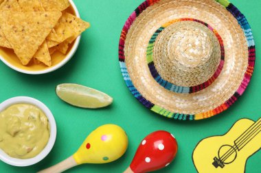 Meksika şapkası, nachos cipsi, guacamole, maracas, yeşil arka planda limon ve kağıt gitar, düz uzanma