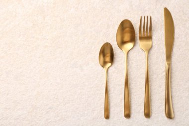 Açık dokulu masa üzerine serilmiş şık altın çatal bıçak seti. Metin için boşluk