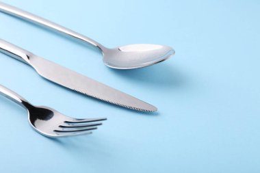 Açık mavi arka planda gümüş çatal bıçak seti, yakın plan. Metin için boşluk