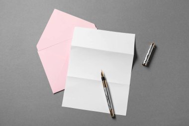 Boş kağıt, mektup zarfı ve gri arka planda kalem, üst görünüm