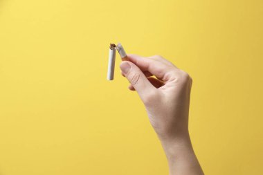 Sigarayı bırak. Sarı arka planda kırık sigara tutan kadın, yakın plan. Metin için boşluk