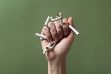Sigarayı bırak. Zeytin arka planında kırık sigara tutan adam, yakın plan.