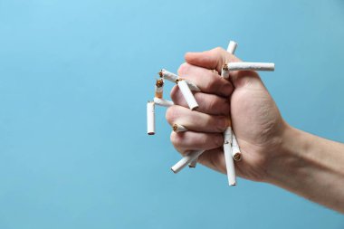 Sigarayı bırak. Açık mavi arka planda kırık sigara tutan adam, yakın plan. Metin için boşluk