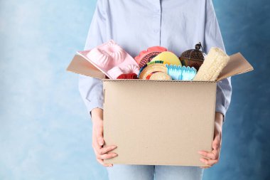 Mavi arka planda istenmeyen eşyalarla dolu bir kutu tutan kadın, yakın plan. Metin için boşluk