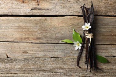Bir sürü vanilya kabuğu, çiçekler ve yapraklar ahşap masa, üst manzara. Metin için boşluk