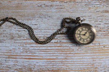 Eski ahşap masada zincirli cep saati, üst manzara.
