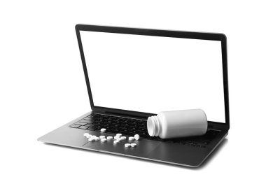 Laptop, ters çevrilmiş şişe ve beyaza izole edilmiş haplar.