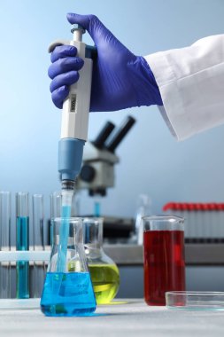 Laboratuvar analizi. Bilim adamı numuneyi mikro pipetle kapalı mekandaki şişeye damlatıyor.