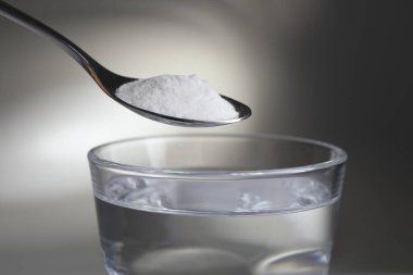 Işık arkaplanındaki bir bardak suyun üzerine kabartma tozu ile kaşık yakın plan.