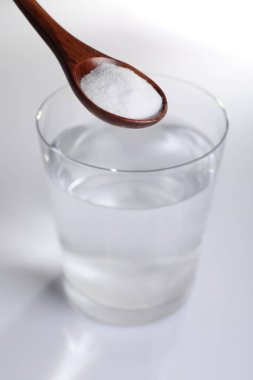 Beyaz zemin üzerinde su bardağı üzerinde kabartma tozu ile kaşık, yakın çekim