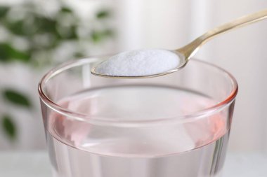 Spoon with baking soda over glass of water on blurred background, closeup clipart