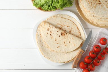 Lezzetli ev yapımı tortilla, domates, marul ve bıçak beyaz ahşap masa, üst manzara. Metin için boşluk