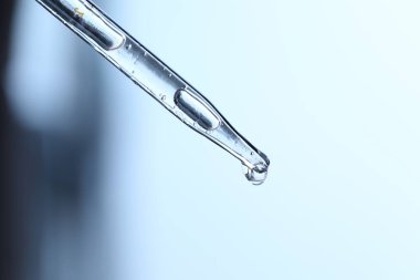 Açık mavi arkaplanda pipetten damlayan sıvı, yakın plan