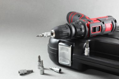 Elektrikli tornavida, matkap uçları ve gri arka planda bir kasa. Metin için boşluk