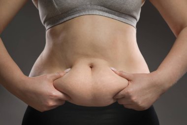 Gri arka planda göbek yağına dokunan kadın, yakın plan. Aşırı kilolu