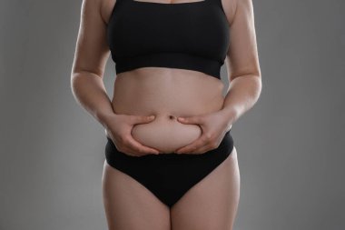 Gri arka planda göbek yağına dokunan kadın, yakın plan. Aşırı kilolu