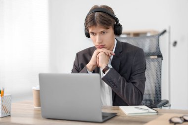 Kulaklıklı bir adam ofisteki ahşap masada Webinar izliyor.