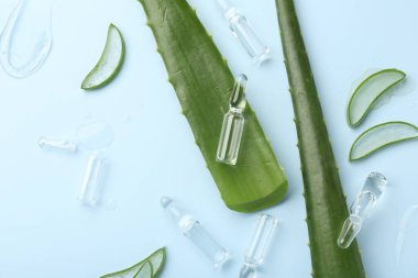 Açık mavi arkaplan üzerinde cilt ampulleri ve aloe yaprakları ile düz konum