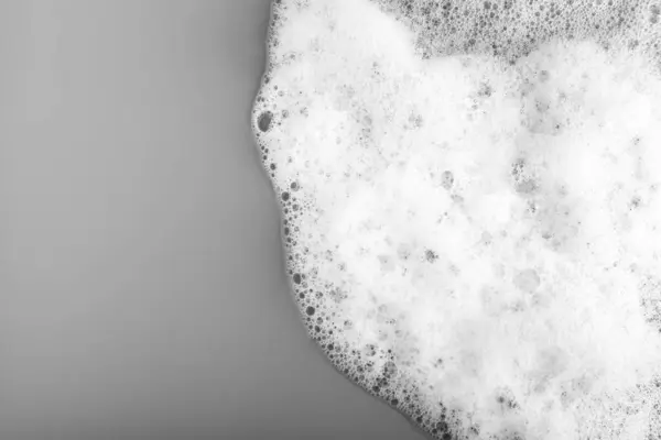 White foam with bubbles on grey background, top view. Space for text