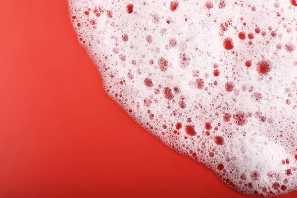 White foam with bubbles on red background, top view. Space for text