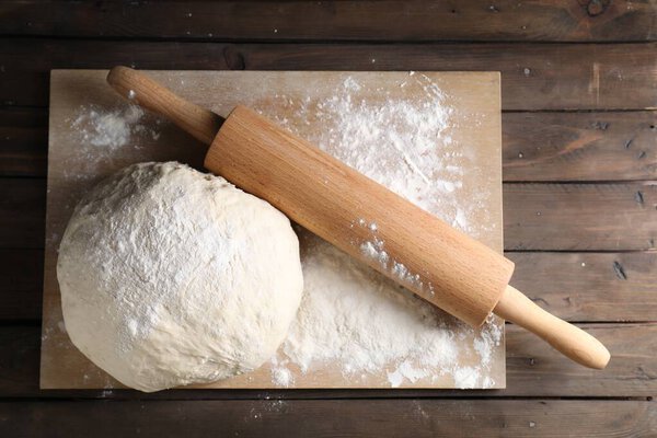 Raw dough and rolling pin on wooden table, top view