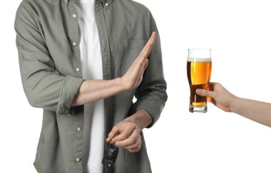 Araba anahtarlı bir adam alkolü reddederken bir kadın ona beyaz arka planda bira öneriyor, yakın plan. İçkili araba kullanma.