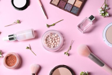 Farklı makyaj ürünleri ve pembe arka planda güzel bahar çiçekleri içeren düz bir kompozisyon.