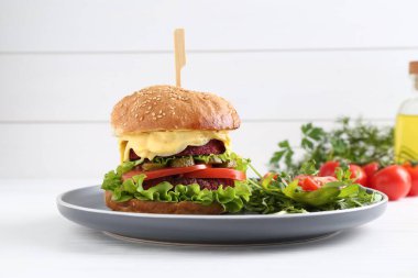 Beyaz ahşap masada salata ile servis edilen lezzetli vejetaryen burger.