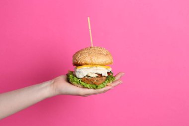 Pembe arka planda nefis vejetaryen burger tutan kadın, yakın plan.