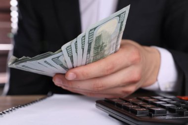 Para değişimi. Tahta masada elinde dolar banknotları tutan adam, yakın plan.