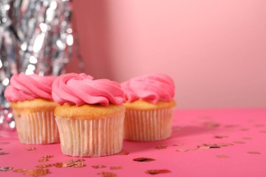 Parlak kremalı lezzetli kekler ve pembe arka planda konfeti. Mesaj için yer var.