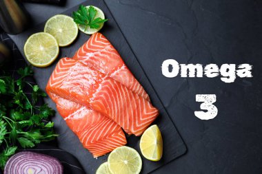 Omega 3. Taze kesilmiş somon, maydanoz, limon ve soğan siyah masada.